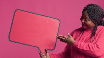 African American beauty holding a red speech bubble mockup for text messages and notes in her right hand. Black lady nodding in agreement with the content of the word-bubble copyspace template. photo