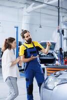 Adept repairman in repair shop using holographic AR technology to show customer car performance parameters. Garage worker using futuristic vr headset to inform client of issues found in vehicle photo