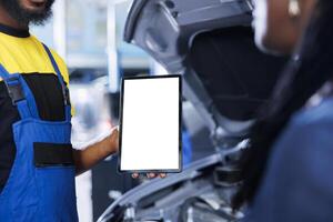 Repairman in car service uses mockup tablet to order new compressor belt for broken vehicle. Employee showing client needed components replacement on isolated screen device, close up photo