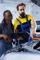 Mechanic in car service uses laptop to calculate invoice after fixing broken automobile distributor. Certified auto repair shop worker uses device to inform woman of final costs after mending vehicle photo