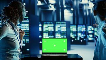 IT developers running code on green screen laptop, troubleshooting data center equipment. Technicians using chroma key device to monitor server cabinets, networking systems and storage arrays photo