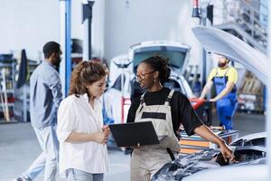 Precise mechanic at auto repair shop conducts annual vehicle checkup, informing client about needed engine replacement. Garage professional talks with customer after finishing car inspection photo