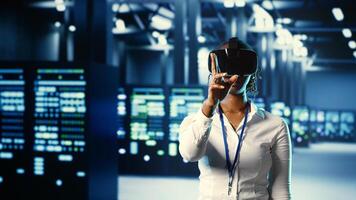 African american trained admin immersed in virtual reality at data center, doing units maintenance. Capable expert using VR headset to optimize servers performance, checking operations photo