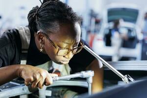 African american engineer does client car maintenance in auto repair shop using lamp light after vehicle shut down unexpectedly. Trained expert in garage mending customer damaged automobile fuel tank photo