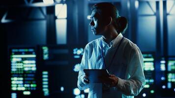 Asian employee walking through data center equipment clusters providing processing resources for different workloads. Productive engineer examining server rigs tasked with solving complex operations photo