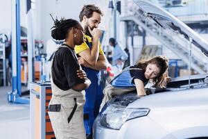 Team of mechanics in auto repair shop working together on fixing car, discussing best options. Multiethnic employees collaborating on servicing broken vehicle, checking for fuel tank photo