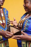 Broke couple discussing bankruptcy and holding purse with no money cash in hands. Smiling black wife showing empty wallet and explaining financial problem to husband closeup photo