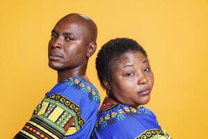 Serious black man and woman standing back to back closeup portrait. African american man and woman looking at camera with serious expression while posing together in studio photo