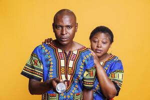 Frightened african american man and woman couple illuminating with flashlight. Confident husband with spotlight searching dark and looking at camera while terrified nervous wife hiding behind back photo