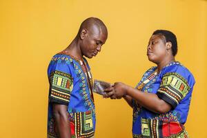 Frustrated african american woman showing empty wallet to sad husband. Displeased poor black couple wearing ethnic clothes having bankruptcy problem and financial difficulties photo