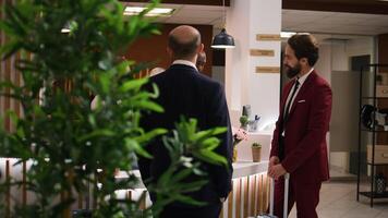 Entrepreneur chats with receptionist in lobby, expressing gratitude to hotel staff members for luxury assistance and services. Businessman appreciating easy check in process on work trip. photo