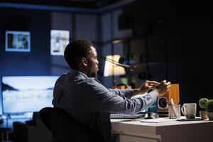 Young man writing sticky notes reminders while studying business administration and management, trying to research and learn economy knowledge. Student attends online classes program. photo