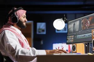 Middle Eastern employee editing video content on multimedia software seen on his computer screen. Side-view shot of male filmmaker working on movie montage edit on the pc monitor. photo