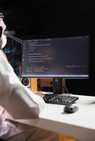 Muslim guy sits at desk and codes on computer, demonstrating the app development process. Over-the-shoulder shot of pc monitor exhibiting running algorithms produced by Arab man dressed traditionally. photo