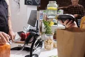 Close up of merchant at checkout counter in zero waste shop selling vegan products to environmentally conscious customers. Client buys healthy food with no additives in local neighborhood store photo