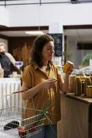 Green living woman in zero waste store interested in purchasing pesticides free produce with high nutritional value. Client does food shopping in environmentally friendly local neighborhood shop photo