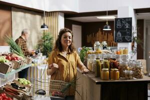 Portrait of cheerful woman looking for locally grown vegetables in eco friendly zero waste store. Hipster client doing grocery shopping, buying organic vegan food items in local neighborhood store photo