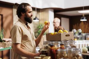 Man in zero waste store taking time to analyze fruits, making sure they are handpicked and farm grown. Green living customer thoroughly checking local supermarket food items are ethically sourced photo