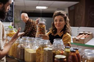 Seller offering customer information about product in environmentally responsible zero waste store. Storekeeper helping client looking for homemade pasta in local neighborhood shop photo