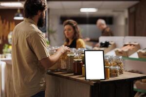 Mockup tablet with empty copy space used as advertising sign in zero waste supermarket with customers shopping for healthy food in blurry background. Isolated screen device in grocery shop photo