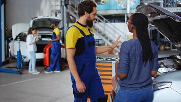 Teamworking colleagues in garage workspace fixing car for customers, thoroughly checking underneath vehicle hood. Mechanics doing routine maintenance on automobile in auto repair shop photo