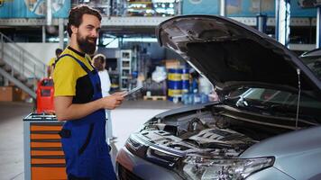 Portrait of licensed technician in auto repair shop doing car routine checkup using tablet, looking for damages. Certified mechanic in garage checking to see if vehicle components need to be changed photo