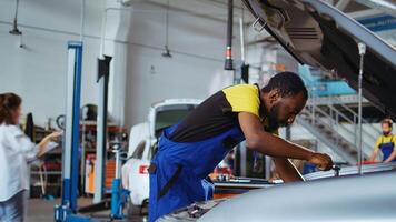 Trained technician in car service picks torque wrench from work station bench, using it to tighten bolts after replacing engine. BIPOC garage worker fixing customer automobile photo
