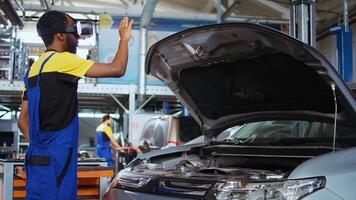 African american repairman employee in garage uses simulating virtual reality glasses to visualize car components in order to fix them. Mechanic wears vr headset while working on out of order vehicle photo