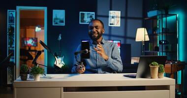 Influencer using selfie stick smartphone, doing video for viewers showing his neon lit apartment studio. Media star talking with followership during live internet stream using mobile phone camera photo