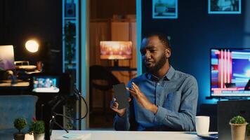 African american tech content creator filming review of newly released smartphone, unboxing it and presenting specifications to audience. Internet star showing phone recommendation to subscribers photo