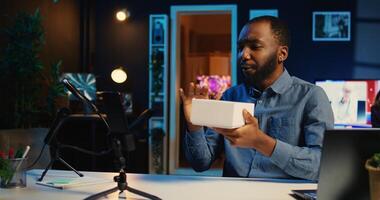 Tech content creator filming packaged product unboxing, unpacking it and presenting specifications to audience. Influencer showing sponsoring brand merchandise to subscribers photo