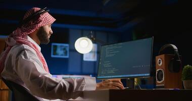 Arab technician writing script code on computer screen inputting commands on terminal. Middle Eastern teleworking employee at home working on fixing company internal database errors photo