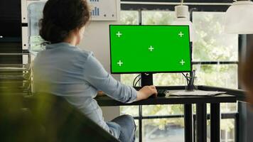 Specialist watches greenscreen desktop sitting at office desk, checking blank chromakey display on monitor. Woman typing information and looking at isolated mockup layout on computer. photo