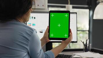 Office worker examines greenscreen layout in coworking space, working on business operations and looking at isolated chromakey display. Woman holding tablet with blank copyspace. photo