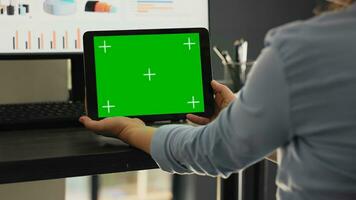 Worker examines greenscreen on tablet in agency coworking space office, looking at chromakey screen with isolated copyspace on mobile gadget. Employee holding chromakey device. photo