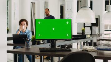 Monitor with greenscreen on empty desk in modern coworking space, pc showing isolated mockup template with copyspace. Device with chromakey display used for small business operations. Tripod shot. photo