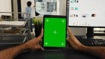 POV of businessman holding tablet with greenscreen template, looking at chromakey display and sitting coworking space desk. Person examining isolated mockup copyspace on gadget screen. photo