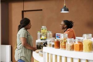 Vendor assisting female client with nutritious products. Cashier at eco friendly store promotes healthy lifestyle, offering fresh locally grown organic produce and sustainable, zero waste options. photo