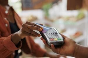 Black person using credit card to make contactless payment for fresh organic produce at a local market. Closeup of african american customer doing cashless transaction at grocery store photo