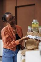 African American woman pays for her bio food using contactless payment on her mobile device. She holds a smartphone and supports cashless transactions at the locally grown market. photo