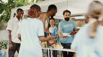 African american female volunteer helping a man using crutches with his meal and nourishments. At a food drive, poor, less fortunate, and homeless people get hunger relief assistance. photo