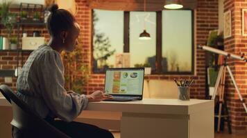 Self employed worker analyzing sales from home office, trying to finish important tasks on freelance network and answer emails. Woman operating software at sunset in apartment. photo