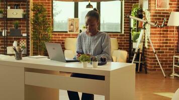 Woman teleworker scrolling webpage and checking social media before starting daily freelance tasks, network connection. African american self employed person sitting at desk at sunset. photo