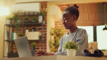 African american woman works at home during sunset hour, publishing blog article on personal website. Freelancer seeking to build online e business while refining abilities. Handheld shot. photo