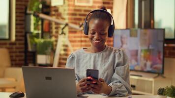 Teleworker browsing online site on phone, taking break from online freelancing tasks during sunset hour. African american person using smartphone social media app at home office. photo