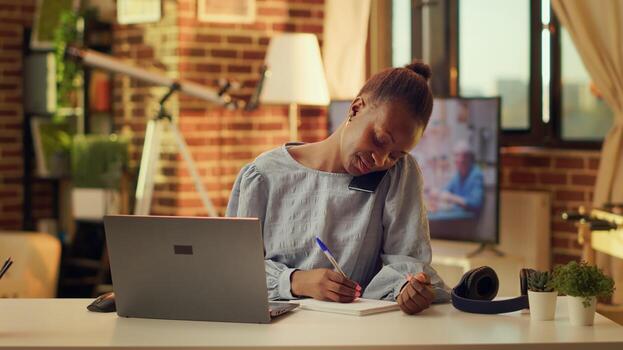 Freelancer writing notes from phone call at home office, using handwriting to have list of information about future tasks. Woman using notebook to create perfect project. photo