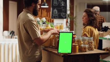 Client shops next to chroma key tablet with copy space used as commercial sign in zero waste supermarket. Promotional ad on green screen device in food store with products in nonpolluting package photo