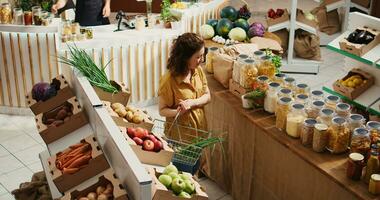 Zero waste store customer roaming around aisles adding healthy natural pantry staples to shopping basket, aerial drone shot. Local grocery shop client buying preservatives free bulk food items photo