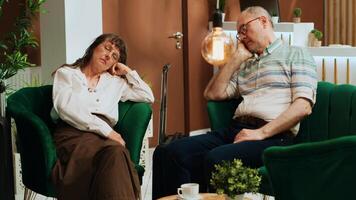 Tired old people falling asleep on sofa at hotel, feeling exhausted because of jetlag and travelling by plane. Retired couple being sleepy and napping in lounge area before check in. Handheld shot. photo