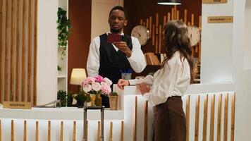 Hotel receptionist assists woman with check in, verifying identity on passport and retrieving reservation details. African american worker checks personal document of tourist at resort. photo
